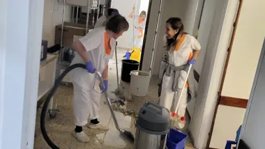 Una fotografía del personal del Hospital Puerta del Mar limpiando el suelo tras una fuga de agua en el área de paritorios, con cubos, fregonas y material sanitario alrededor. Escena realista y tensa que refleja el impacto del incidente en plena jornada asistencial.