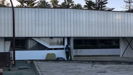 Imagen de la Pérgola de Santa Bárbara en Cádiz. En primer plano se ven cartones, mantas y ropa extendida en el suelo. Una pareja busca refugio. La escena transmite vulnerabilidad y falta de un lugar seguro donde dormir.