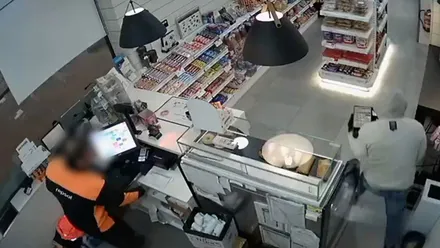 Dependiente de la gasolinera y el ladrón huyendo a su derecha con chaleco gris.