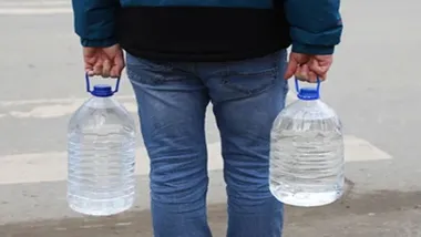 Persona en vaqueros y con chaquetón portando dos garrafas de agua, una en cada mano.