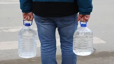 Persona en vaqueros y con chaquetón portando dos garrafas de agua, una en cada mano.