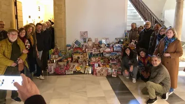 Personas del Ateneo de Jerez junto a muchos juguetes donados y una persona que les hacen una foto con un teléfono móvil.