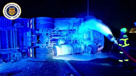 Camión volcado en la carretera siendo refrescado por un bombero.