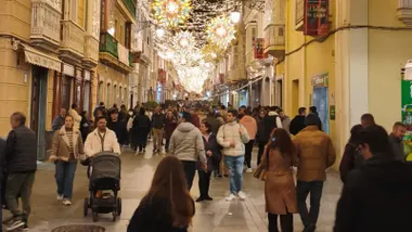 Vista nocturna de la calle Ancha de Cádiz iluminada con luces de Navidad, terrazas abiertas y personas paseando entre la decoración festiva.