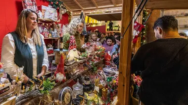 Personas comprando en un mercadillo navideño con diferentes productos.