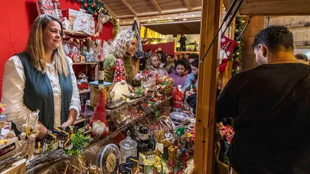 Personas comprando en un mercadillo navideño con diferentes productos.