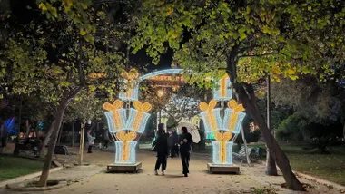 Dos personas asan por debajo de uno de los acros de alumbrado extraordinario de Navidad en la plaza de España. Ambas llevan paraguas y charlan entre ellas.