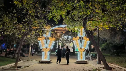 Dos personas asan por debajo de uno de los acros de alumbrado extraordinario de Navidad en la plaza de España. Ambas llevan paraguas y charlan entre ellas.