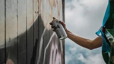 Muchacho con bote de spray pintando sobre un muro de tablas.