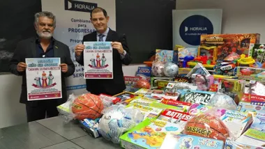 Juguetes y dos personas de Hidralia sosteniendo el cartel de la campaña "Ningún niño sin juguete".