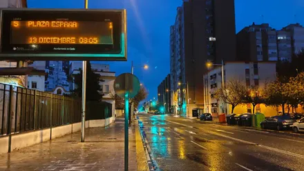 Avenida de la Sanidad Pública de Cádiz con el suelo mojado y un cartel de información de autobuses con la hora de este 13 de diciembre a la que fue tomada la foto: 8:05.