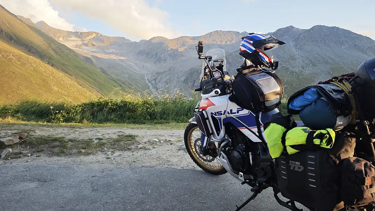 Motocicleta de viaje en una carretera de montaña rodeada de picos nevados, en plena travesía alpina.
