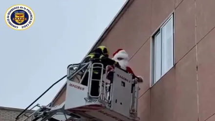 Un bombero junto a Papa Noel en una escalera repartiendo regalos por las ventanas del Hospital de Jerez.