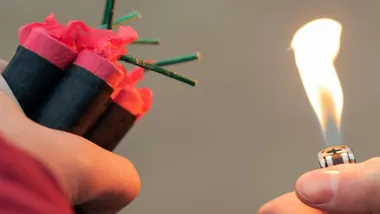 Persona encendiendo con un mechero un grupo de petardos.