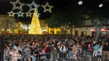 Personas en la Plaza de Puerto Real celebrando las pre-Uvas, con luces navideñas.