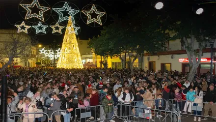Personas en la Plaza de Puerto Real celebrando las pre-Uvas, con luces navideñas.