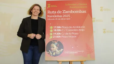 Manuela Pérez presentando la Ruta de las Zambombas en Chiclana posando junto al cartel en rojo.