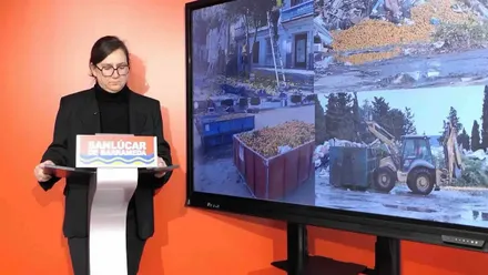 Mónica González junto a una pantalla con diferentes momentos de la recogida de naranjas.