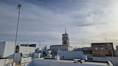 Imagen tomada en Cádiz con un cielo parcialmente despejado, en el que se alternan nubes y claros. El sol ilumina la Torre Tavira, destacando su silueta sobre el casco histórico y transmitiendo una sensación de estabilidad tras varios días de tiempo inestable.