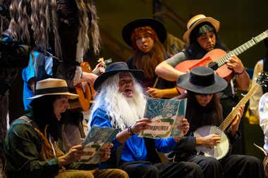 Imagen de la chirigota Los amish sobre el escenario del Gran Teatro Falla, caracterizados con su tipo y cantando durante su actuación en el COAC, bajo la iluminación del teatro y con el público al fondo.