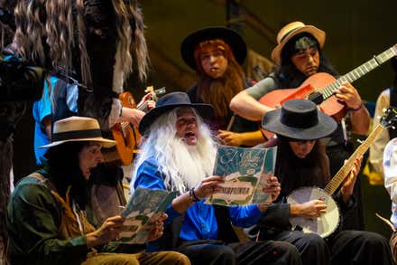 Imagen de la chirigota Los amish sobre el escenario del Gran Teatro Falla, caracterizados con su tipo y cantando durante su actuación en el COAC, bajo la iluminación del teatro y con el público al fondo.