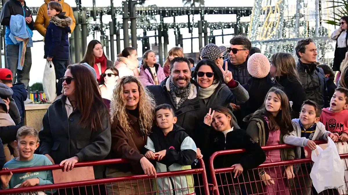 Familias con niños observan la Cabalgata de Reyes Magos desde la acera, en un ambiente festivo y concurrido.