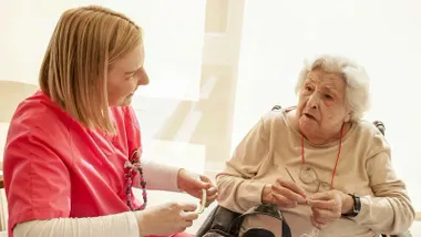 Una mujer mayor en silla de ruedas ayudada por una chica de Ayuda a Domicilio.