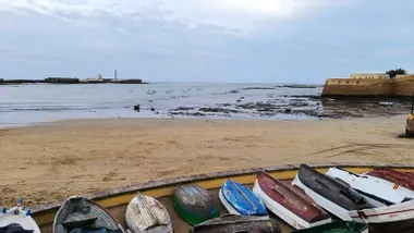Imagen de la playa de la Caleta en bajamar con sus barquitas y sus dos castillos en los que se aprecia como van entrando las nubes de un nuevo frente atlántico
