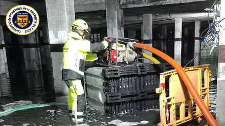 Bombero, con traje amarillo, sacando agua junto a una bomba de achique.