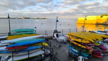Playa de La Caleta, los dos castillos y embarcaciones en el club bajo un cielo con pocas nubes y un mar en calma