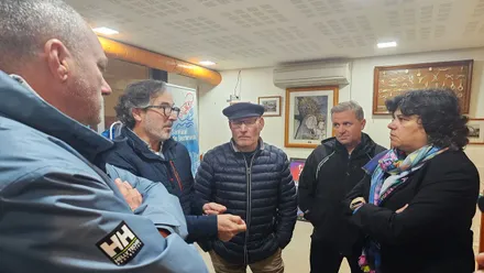 Grupo de pescadores reunidos con la alcaldesa en un salón, conversan con ella.