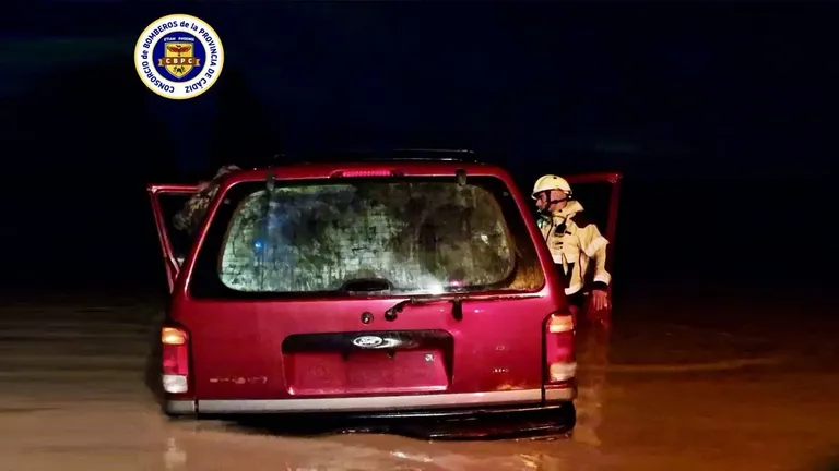 Coche rojo anegado de agua y un bombero revisando el interior.