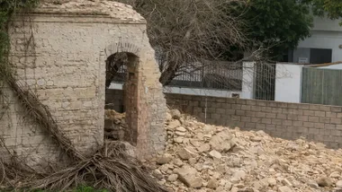 Muro caído del edificio, se observan los escombros y ramas de árboles.