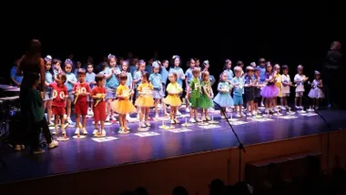 Niños y niñas con vistosos trajes de colores en el escenario del teatro.