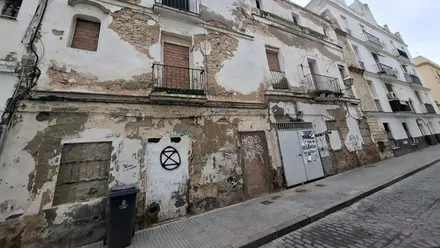 Imagen de un edificio residencial antiguo en la calle Pericón, en el casco histórico de Cádiz. La fachada presenta varias plantas, balcones y puertas cerradas en la planta baja, sin andamios ni maquinaria visible, lo que indica que las obras anunciadas aún no han comenzado.