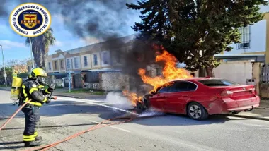 Bombero con manguera y equipo sofocando el incendio en un coche de color rojo.