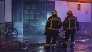 Dos bomberos ante la puerta del garaje incendiado.