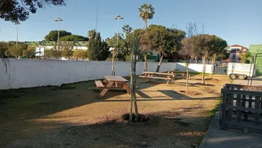 Patio de un colegio con zonas de sombra, bancos y mesas.