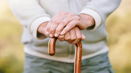 Manos de persona mayor apoyándose en un bastón.
