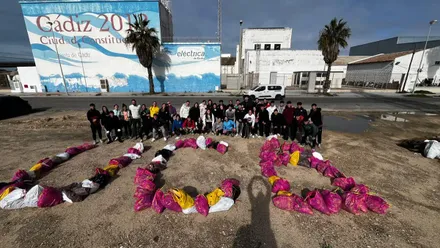 Fotografía tomada al final de la jornada, mostrando a los estudiantes del CAFYD con bolsas repletas frente al mar en la playa de Cortadura, bajo el sol de Cádiz formando el nombre de la UCA