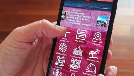 Mano sosteniendo un móvil con la aplicación "Mejora Chiclana".