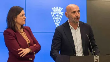 Patricia Cavada con chaqueta burdeos atiende la explicación de Monchi.