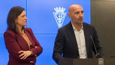 Patricia Cavada con chaqueta burdeos atiende la explicación de Monchi.