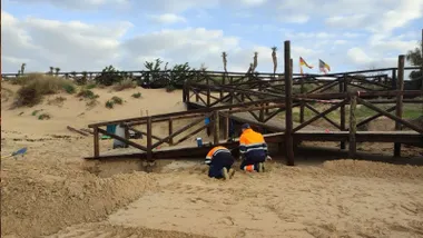 Dos operarios reforzando las pasarelas de las playas de Rota, hechas en madera.