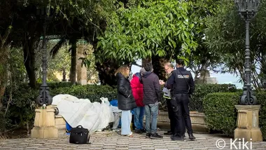 Dos policías y dos personas están ante el cuerpo tapado sobe un banco de la tercera persona sin hogar que fallece en Cádiz en lo que va de año