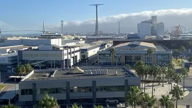 Fotografía tomada desde el aire que muestra el edificio central del Consorcio de la Zona Franca de Cádiz rodeado de instalaciones industriales y naves logísticas. Al fondo se distingue el puerto y parte del litoral gaditano bajo un cielo despejado.