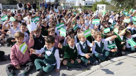 Muchos niños y niñas con banderas de Andalucía sentados celebrando el 28F.