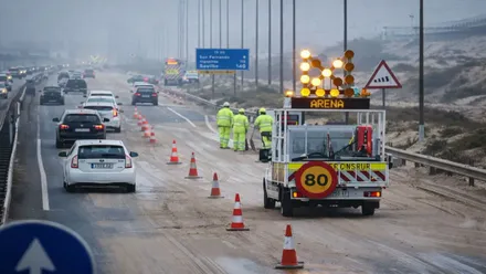 Operarios retirando arena de la carretera y los coches pasando.
