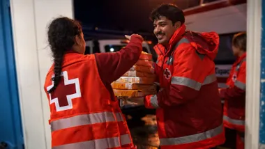 Chica y chico de la Cruz Roja, con el uniforme, cargando cajas de ayuda.