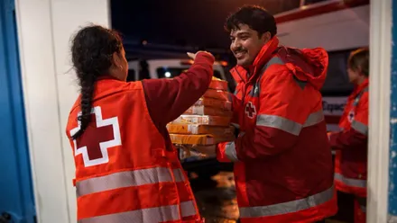 Chica y chico de la Cruz Roja, con el uniforme, cargando cajas de ayuda.